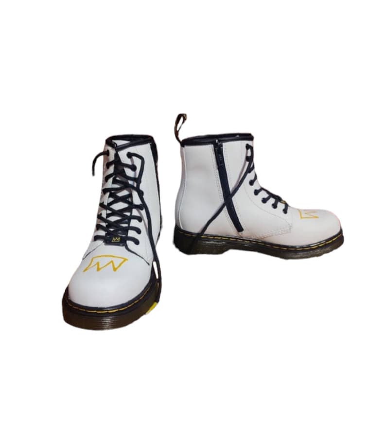 May include: White leather ankle boots with black laces and a yellow crown design. The boots have a black zipper on the side and a black and yellow sole.