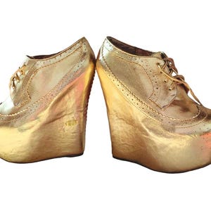 Könnte beinhalten: Ein Paar goldene Plateauschuhe mit Schnürung. Die Schuhe haben einen dicken Keilabsatz und eine abgerundete Spitze.