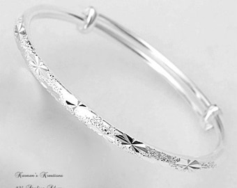 Può includere: Un bracciale rigido regolabile color argento con una superficie testurizzata e incisioni ripetute a forma di stella. Il testo Karmen's Kreations, 925 Sterling Silver e l'URL del sito web sono stampati nell'angolo in basso a sinistra.