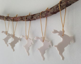 May include: Six white ceramic reindeer ornaments hanging from a branch with gold string. The reindeer are all facing the same direction and are in a row.