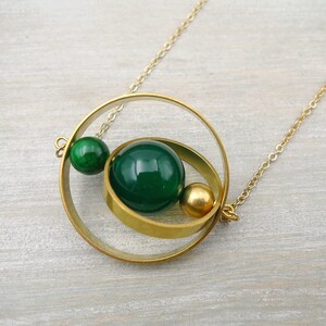 May include: A gold necklace with a circular pendant featuring two green glass beads and a gold bead. The pendant is made of two interlocking circles.