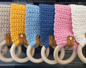 Puede incluir: Conjunto de siete mordedores de crochet en varios colores, incluyendo turquesa, beige, amarillo, azul, rosa y blanco. Cada mordedor tiene un anillo de madera y una etiqueta de cuero con el texto "knot knot" en él.