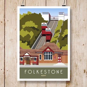May include: A vintage-style illustration of the Folkestone Cliff Railway in Kent, England. The red cable cars ascend a steep incline, with a brick building at the bottom of the hill. The text "FOLKESTONE KENT" is printed below the image.