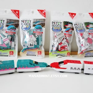 Puede incluir: Cuatro bolsas sin abrir de juegos de construcción japoneses Petit Block para construir trenes bala. Las bolsas contienen bloques de plástico blanco, rojo y verde. Se muestran cuatro trenes bala ensamblados en primer plano. Los trenes son blancos con detalles rojos y verdes.