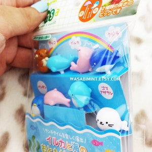 Puede incluir: Un conjunto de ocho pinchos para comida de pl&aacute;stico de colores con una variedad de criaturas marinas, incluyendo delfines, ballenas, ping&uuml;inos y focas. Los pinchos est&aacute;n empaquetados en una bolsa de pl&aacute;stico transparente con un fondo colorido y el texto "イルカと海の おともだちピック 8本入" en japon&eacute;s.