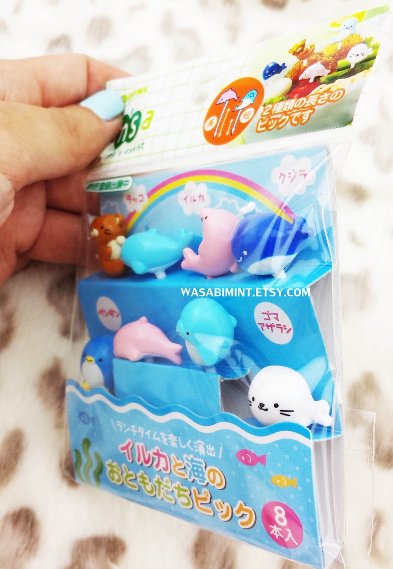 Puede incluir: Un conjunto de ocho pinchos para comida de pl&aacute;stico de colores con una variedad de criaturas marinas, incluyendo delfines, ballenas, ping&uuml;inos y focas. Los pinchos est&aacute;n empaquetados en una bolsa de pl&aacute;stico transparente con un fondo colorido y el texto "イルカと海の おともだちピック 8本入" en japon&eacute;s.