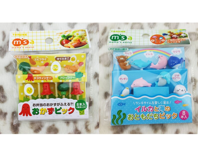 Puede incluir: Dos paquetes de pinchos para comida coloridos. El primer paquete contiene ocho pinchos con dise&ntilde;os de pulpo, huevo, br&oacute;coli y camar&oacute;n. El segundo paquete contiene ocho pinchos con dise&ntilde;os de ping&uuml;ino, foca, delf&iacute;n y oso. El texto en el primer paquete dice "Okazu Bick" y el texto en el segundo paquete dice "Iruka to Umi no Otomo Dachi Pick".