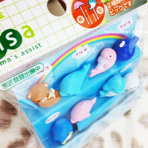 Puede incluir: Un conjunto de pinchos para comida de pl&aacute;stico de colores con una variedad de criaturas marinas, incluyendo delfines, ballenas y un ping&uuml;ino. Los pinchos est&aacute;n empaquetados en una bolsa de pl&aacute;stico transparente con un dise&ntilde;o de arco&iacute;ris y el texto "m'sa mama's assist" y "意匠登録出願中".