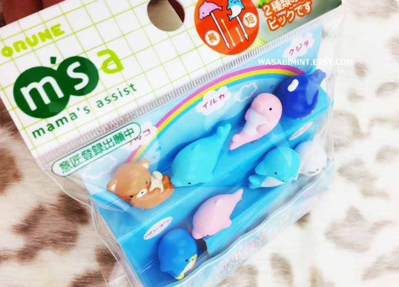 Puede incluir: Un conjunto de pinchos para comida de pl&aacute;stico de colores con una variedad de criaturas marinas, incluyendo delfines, ballenas y un ping&uuml;ino. Los pinchos est&aacute;n empaquetados en una bolsa de pl&aacute;stico transparente con un dise&ntilde;o de arco&iacute;ris y el texto "m'sa mama's assist" y "意匠登録出願中".