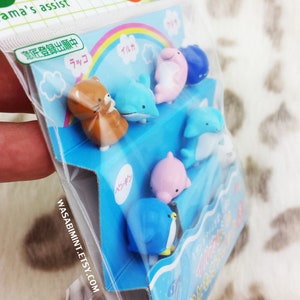 Puede incluir: Una bolsa de pl&aacute;stico transparente que contiene un juego de pinchos para comida con forma de animales de colores. Los pinchos est&aacute;n dispuestos en una caja azul y blanca con texto japon&eacute;s. Los pinchos incluyen un ping&uuml;ino, un delf&iacute;n, una foca y un oso.