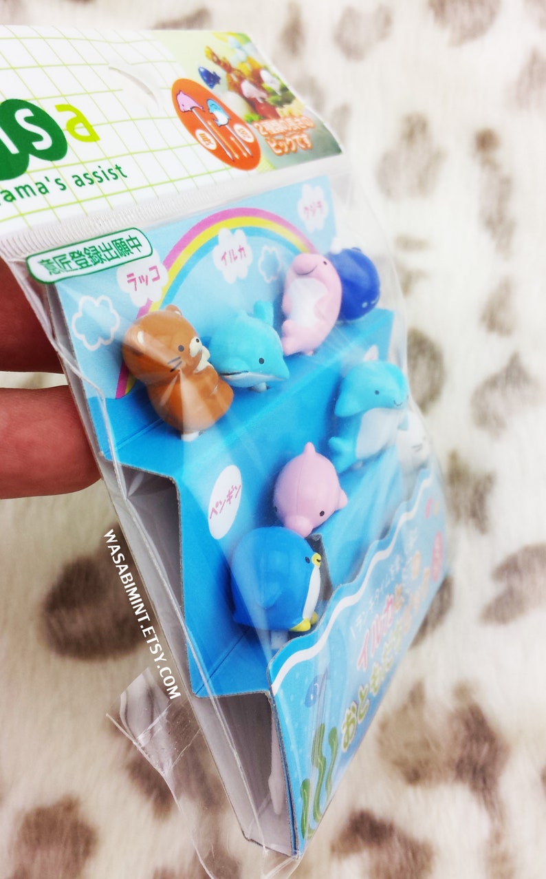 Puede incluir: Una bolsa de pl&aacute;stico transparente que contiene un juego de pinchos para comida con forma de animales de colores. Los pinchos est&aacute;n dispuestos en una caja azul y blanca con texto japon&eacute;s. Los pinchos incluyen un ping&uuml;ino, un delf&iacute;n, una foca y un oso.