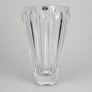 May include: A clear, colorless glass vase with a flared, wide opening and a tapered base. The exterior features vertical, faceted cut patterns that create a series of sharp, angular ridges. A small, circular blue and gold Bohemia sticker is attached.