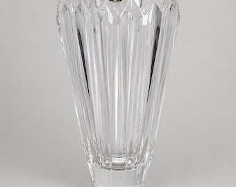 May include: A clear, colorless glass vase with a flared, wide opening and a tapered base. The exterior features vertical, faceted cut patterns that create a series of sharp, angular ridges. A small, circular blue and gold Bohemia sticker is attached.