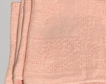 May include: A set of folded light peach-colored napkins featuring a delicate openwork lace border and a subtle embroidered floral pattern along the edges. The fabric has a visible woven texture and a soft, matte finish throughout the square pieces.