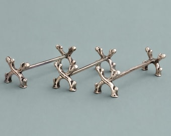 May include: Three silver-colored metal chopstick rests, each featuring a central horizontal bar connected to two X-shaped supports at either end. The supports have a textured, branch-like appearance with rounded tips and a polished metallic finish.