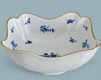 May include: A white porcelain bowl with a scalloped edge and a gold-painted rim. The interior and exterior surfaces are decorated with small, scattered blue floral sprigs and a larger blue floral cluster at the center of the bowl base.