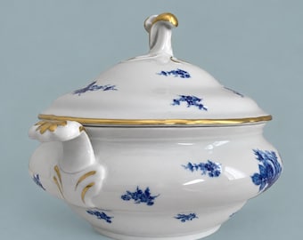 May include: A white porcelain tureen with a matching lid, featuring delicate blue floral patterns scattered across the surface. The piece is accented with gold trim along the rim and handles, and includes a sculpted handle on the lid.