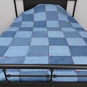 May include: A black metal bed frame with a headboard and footboard featuring decorative finials. The bed is covered by a patchwork quilt made of square denim fabric panels in varying shades of blue, joined with visible red stitching at corners.