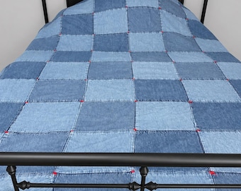 May include: A black metal bed frame with a headboard and footboard featuring decorative finials. The bed is covered by a patchwork quilt made of square denim fabric panels in varying shades of blue, joined with visible red stitching at corners.