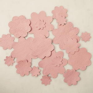 May include: A collection of pink leather flower shapes, some with scalloped edges, arranged on a white background.