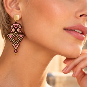 May include: A geometric drop earring featuring a small gold square stud connected to a larger, intricate pendant crafted from tiny black, pink, and white beads arranged in a symmetrical, pointed diamond-like pattern with a small gold bead at the base.