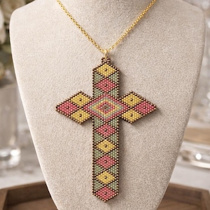 Può includere: Collana con pendente a croce di perline e catena dorata. Il design della croce utilizza perline rosa, gialle e verdi in un motivo geometrico. La collana è esposta su un busto di manichino.