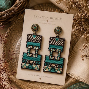 Könnte beinhalten: Handgefertigte Ohrringe mit geometrischem Design in Türkis, Schwarz und Creme. Auf der Karte steht "PATRIZIA BIJOUX HANDMADE WITH LOVE" und "FATTO A MANO CON PASSIONE". Die Ohrringe haben bronzefarbene Metalldetails.