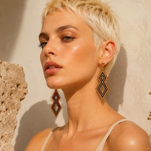 Può includere: Orecchini dorati con un design geometrico a forma di diamante. Gli orecchini presentano perline nere e arancioni, creando un contrasto sorprendente. Gli orecchini sono pendenti, aggiungendo movimento e interesse visivo.