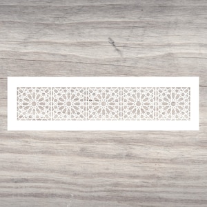 May include: A white stencil featuring a repeating geometric pattern. The design is composed of intricate star and line arrangements, creating a symmetrical and decorative border. The stencil is rectangular and rests on a wooden surface.