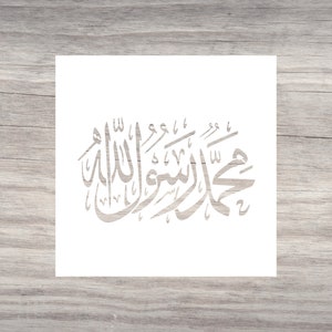 May include: A white square featuring light grey Arabic calligraphy. The calligraphy is centrally positioned and displays graceful, flowing script. The background has a light wood grain pattern.