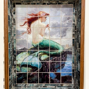 Può includere: Un mosaico di piastrelle incorniciato che raffigura una sirena con lunghi capelli rossi seduta su uno scoglio. La sirena indossa una coda verde e tiene una conchiglia. Lo sfondo è un cielo nuvoloso con una città in lontananza.