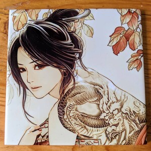 Puede incluir: Un azulejo de cerámica con fondo blanco que presenta a una mujer con el pelo largo y negro, vestida con un kimono japonés tradicional con un tatuaje de dragón en el brazo. La mujer tiene una expresión seria y mira hacia un lado. El fondo presenta un diseño floral estilizado en tonos marrones y rojos.