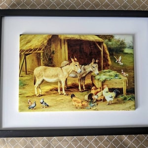 May include: A framed painting of two donkeys standing in front of a barn with a thatched roof. The donkeys are brown and white and are eating hay. There are chickens and pigeons in the foreground.