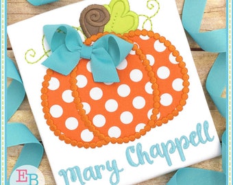 May include: A white t-shirt with an orange and white polka dot pumpkin with a blue bow and green leaves. The name "Mary Chappell" is embroidered in blue below the pumpkin.