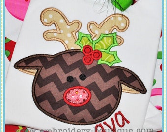 May include: Embroidered design of a brown reindeer with a red nose and green holly on a white background. The reindeer has a chevron pattern and the text "Ava" is embroidered below the reindeer.
