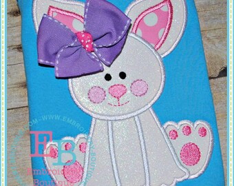 May include: White bunny applique with a purple bow and pink polka dot ears. The bunny is sitting with its paws visible. The applique is on a blue background.