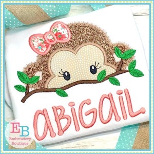 May include: Embroidered design of a monkey wearing a pink bow with floral print, peeking over a branch with green leaves. The name "Abigail" is embroidered in pink below the monkey.