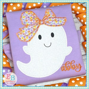 May include: Purple shirt with a white ghost wearing a floral bow and the name "Abby" embroidered in orange.