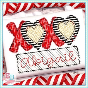 May include: Red, black, and white embroidered design of the letters "XO" with two hearts. The hearts have a black and white striped pattern and a gold leopard print inside. The design is on a white shirt with a black and white polka dot banner below that says "Abigail".