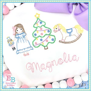 May include: Embroidered design featuring a girl holding a nutcracker, a Christmas tree with ornaments, and a rocking horse. The name "Magnolia" is embroidered below the design.