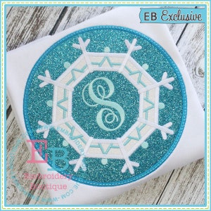 May include: A blue and white snowflake design with a white letter "S" in the center. The design is on a white background and has a glittery texture. The text "EB Exclusive" is in the upper right corner of the image.