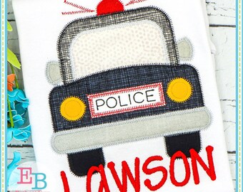 May include: A black and gray police car with a red light on top and the word "POLICE" on the side. The car is embroidered on a white fabric with the name "LAWSON" in red lettering below.