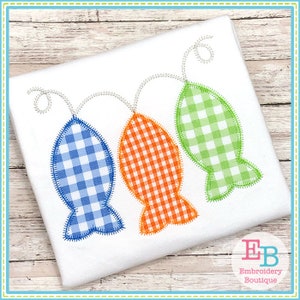 May include: Three embroidered fish in blue, orange, and green gingham patterns are strung together with a white thread. The fish are on a white fabric background.
