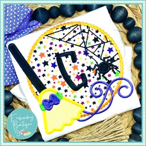 May include: A white t-shirt with a black letter C, a black spider, and a yellow and orange broom with a purple bow. The design is surrounded by a circle of orange and yellow stars and a spider web.