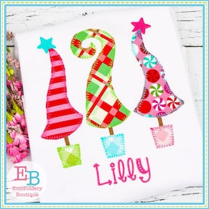 May include: Three colorful patchwork Christmas trees with star toppers and the name "Lilly" embroidered in pink below.