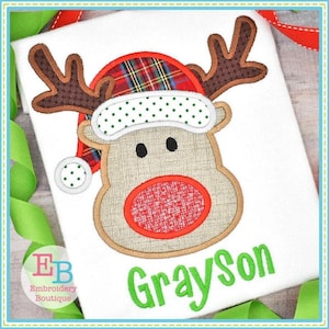 May include: A white t-shirt with a brown and red applique of a reindeer wearing a plaid Santa hat. The reindeer has a red nose and brown antlers. The name Grayson is embroidered in green below the reindeer.