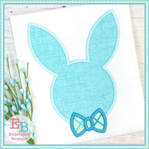 May include: A light blue bunny applique with a green and white bow tie. The bunny is outlined in white and has a textured fabric design.