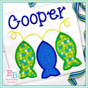 May include: Embroidered design of three fish with a yellow, green, and blue pattern. The name "Cooper" is embroidered above the fish.