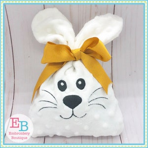 May include: White bunny-shaped fabric gift bag with a yellow bow. The bag has embroidered eyes, nose, and whiskers.