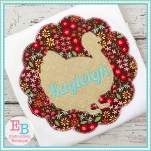 May include: A brown and white turkey silhouette with a scalloped edge, surrounded by a floral pattern in shades of red, orange, yellow, and green. The name "Kayleigh" is embroidered in teal on the turkey's body.